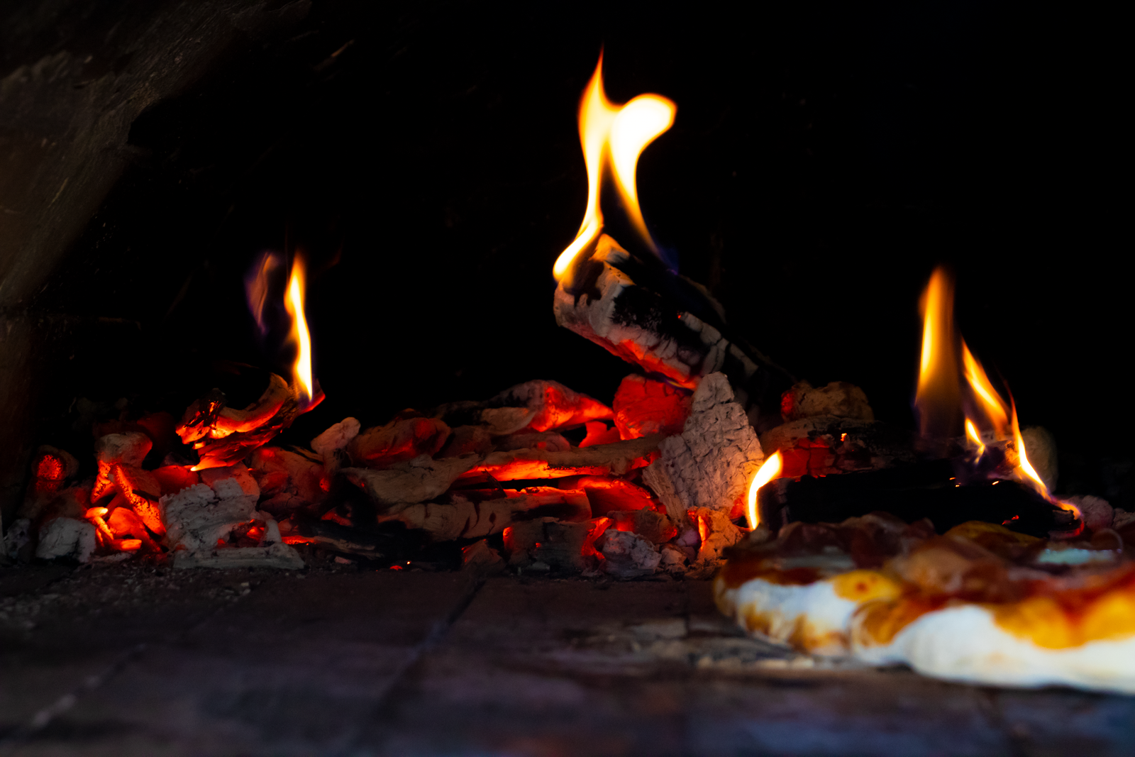 A close-up of a stone oven with bright flames, showcasing the baking process of a pizza.