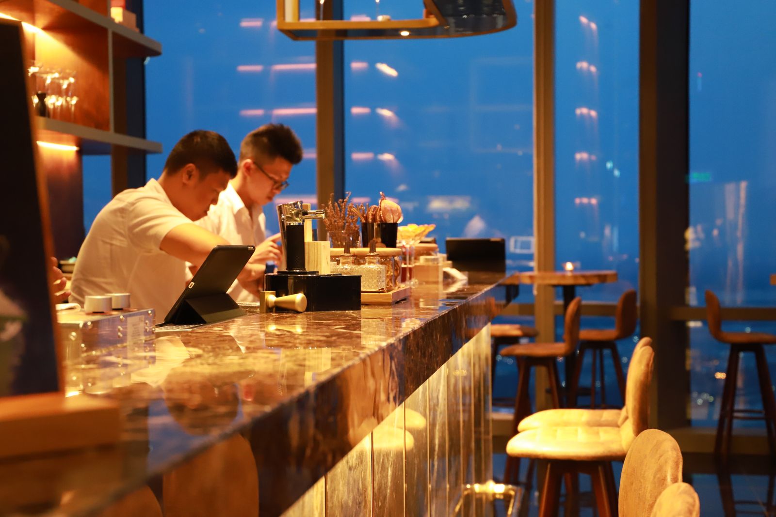 Two men working at a stylish bar counter in Hồ Chí Minh City with a city view.